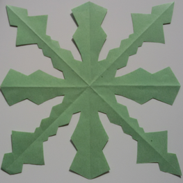 Foto eines Faltschnittes aus grünem Papier. Entstanden ist eine Schneeflocken-ähnliche Form.