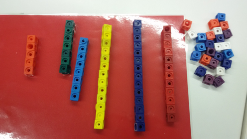 Foto zum Zählen von Steckwürfeln. Rechts: unstrukturierte Menge an Steckwürfeln. Links: 6 unterschiedlich lange Türme mit Steckwürfeln jeweils einer Farbe.
