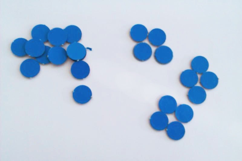Foto von blauen Plättchen, die links ungeordnet auf einem Haufen liegen und rechts zu 3 Gruppen mit jeweils 4 Plättchen sortiert wurden.