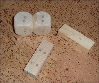 Foto von selbst erstellten Würfeln mit rechteckiger Form aus einem Holzstück beziehungsweise zusammengeklebt aus zwei sechsflächigen Würfeln mit aufgezeichneten Würfelaugen.