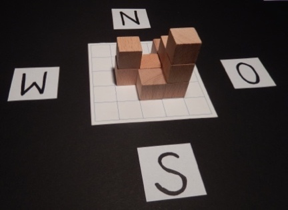 Foto eines Würfelgebäudes, das auf einem Planungsraster steht. Dieses wurde mit „N“, „O“, „S“ und „W“ entsprechend der Himmelsrichtungen beschriftet.