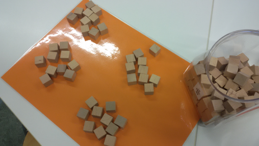 Foto zum Zählen von Holzwürfeln. Rechts: Glas mit vielen Holzwürfeln. Links: 4 Haufen mit jeweils 10 Holzwürfeln.